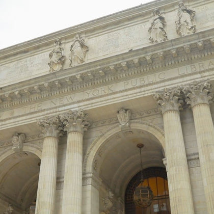 Facade of the New York Public Library with columns, arches, and statues under a cloudy sky.
