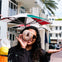 A woman holding a doughnut with a hole up to her eye, standing beside an ice cream cone statue outside an ice cream shop.