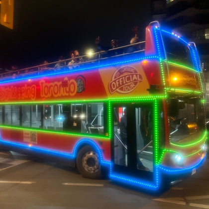 Open top double decker bus turning a corner at night time. Bus is covered with LED lights