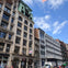 A city street with historic multi-story buildings, a truck parked, and pedestrians under a partly cloudy sky.