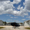 A black helicopter sits on a runway between two hangars under a cloudy blue sky.