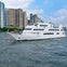 A large white passenger boat on a city river, with tall buildings and a blue sky in the background.