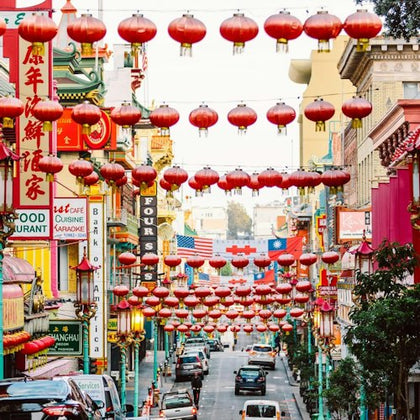 A street decorated with rows of red lanterns, colorful signs on buildings, and cars driving below.