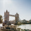 Tower Bridge over the River Thames on a sunny day, with surrounding architecture and water reflections visible.