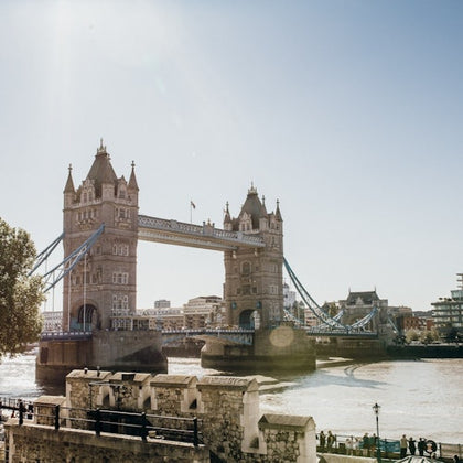 Tower Bridge over the River Thames on a sunny day, with surrounding architecture and water reflections visible.