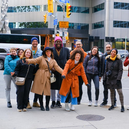 A group of people smiling and posing together on a city sidewalk with buildings and traffic signs in the background.