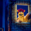A puppet with orange fur, red hair, and yellow horns looks out from a brick-framed window in a dimly lit scene.
