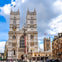 A view of Westminster Abbey with its twin towers, a statue in front, and the surrounding area under a partly cloudy sky.