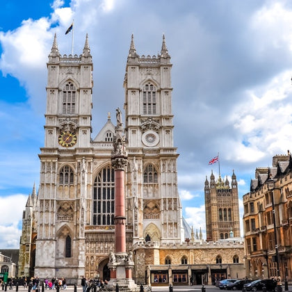 A view of Westminster Abbey with its twin towers, a statue in front, and the surrounding area under a partly cloudy sky.