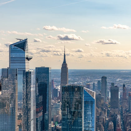 Aerial view of New York City skyscrapers, including the Empire State Building, under a partly cloudy sky.