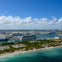 Aerial view of a coastal city with docks, multiple cruise ships, and urban buildings under a partly cloudy sky.