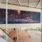 Spacious modern atrium with a large digital mural on the wall, depicting people in a dramatic scene. Two people walk below.