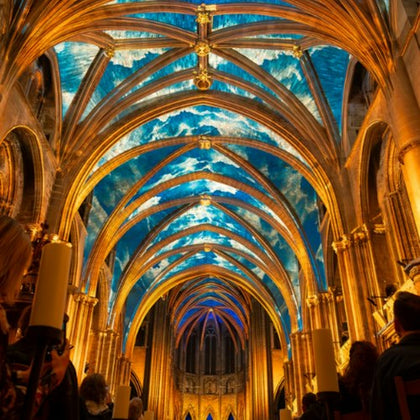 A cathedral interior with illuminated golden arches and a ceiling displaying a vibrant blue sky with clouds.