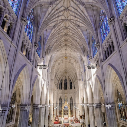 A grand cathedral interior with high vaulted ceilings, stained glass windows, and an ornate altar at the front.