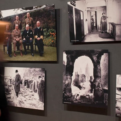 A wall displays five historical photos, including group portraits, scenes of destruction, and a man walking through ruins.