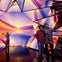People standing in a room with reflective surfaces and vibrant, colorful light patterns resembling a sunset.