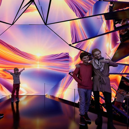 People standing in a room with reflective surfaces and vibrant, colorful light patterns resembling a sunset.