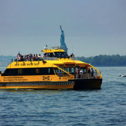 A yellow New York Water Taxi with passengers on board on the water, with the Statue of Liberty visible in the background.