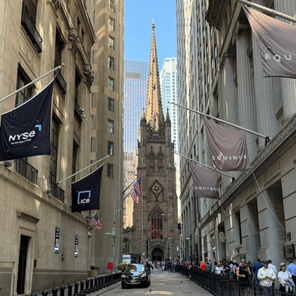 Street view of Wall Street with Trinity Church in the background, surrounded by tall buildings and flags hanging on both sides.