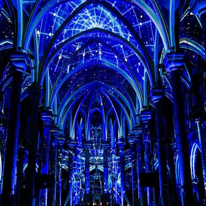 A cathedral interior illuminated with blue light projections resembling constellations and stars on its arches and ceiling.