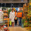 Three people holding shopping bags in a colorful store decorated with plants, shelves, and a lit Christmas tree.