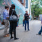 A group of people is gathered in an alleyway with murals on the walls, listening to a man speaking and gesturing animatedly.