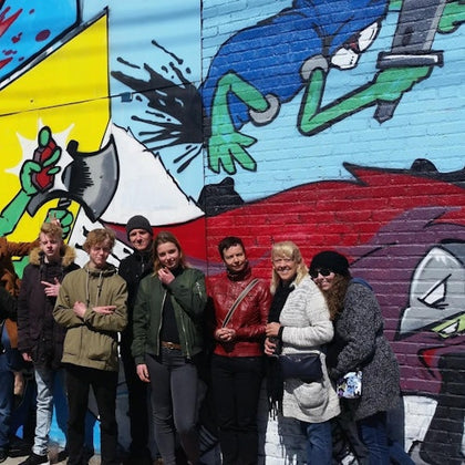 A group of people posing in front of a colorful graffiti wall featuring animated characters and vibrant designs.
