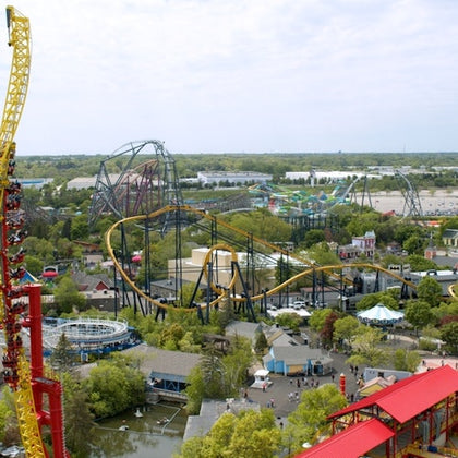 A theme park with multiple roller coasters, rides, buildings, and green trees under a cloudy sky.
