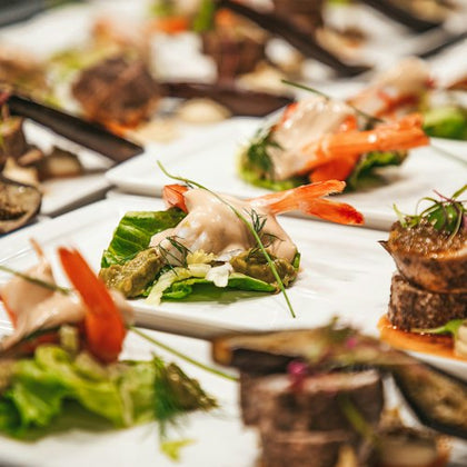 Plates of gourmet appetizers with shrimp, greens, and garnish, arranged neatly on a table.