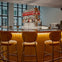 A modern bar with a curved counter, upholstered stools, and shelves displaying various liquor bottles under soft lighting.