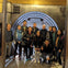 A group of people posing in front of a large, round metal vault door in an interior setting.