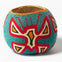 A round decorative object with colorful geometric patterns in red, blue, and white, resembling a handcrafted design.