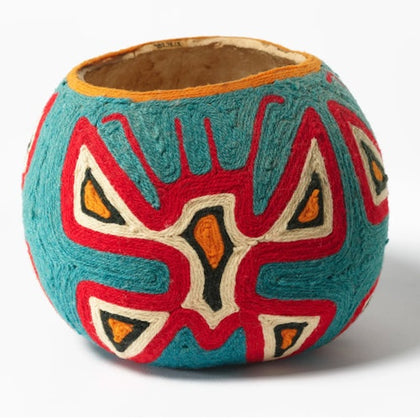 A round decorative object with colorful geometric patterns in red, blue, and white, resembling a handcrafted design.