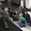 Group of children and adults examining a dinosaur skeleton exhibit in a museum. A woman supports a young child touching a fossil.