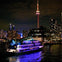 A lit boat on water at night with city buildings and the CN Tower illuminated in the background.