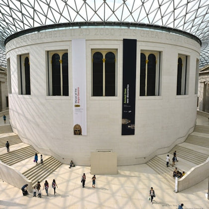 The British Museum's Great Court, featuring a large circular structure, banners on walls, and visitors on surrounding stairs.