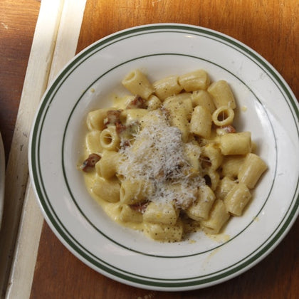 A plate of pasta with cheese and sauce garnished with grated cheese on a wooden table.
