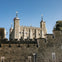 Stone castle with multiple turrets and crenellated walls under a clear blue sky. Trees are visible in the background.