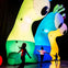 Children playing near large inflatable creatures illuminated in vibrant colors, resembling stylized alien or monster figures.