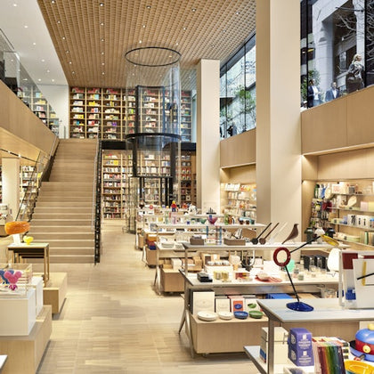 A modern bookstore with wooden shelves, a central staircase, and a variety of books and items on display.