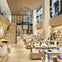 Modern bookstore interior with wooden decor, shelves filled with books, a staircase, and a variety of displayed items.