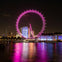 A brightly illuminated Ferris wheel with pink lights, set against a city skyline at night, reflecting on the water below.