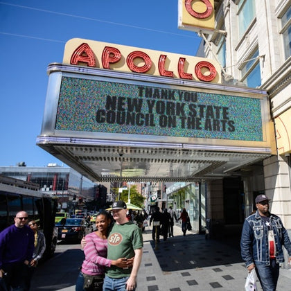 Pedestrians walk under the Apollo Theater marquee, which thanks the New York State Council on the Arts.