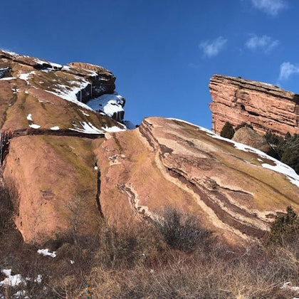 Rugged red rock formations dusted with snow under a clear blue sky; sparse vegetation in the foreground.