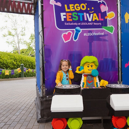 A child posing next to a LEGO DJ model at a LEGO Festival display.