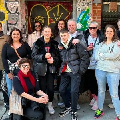 A group of people posing together in front of a graffiti-covered wall on a city street.