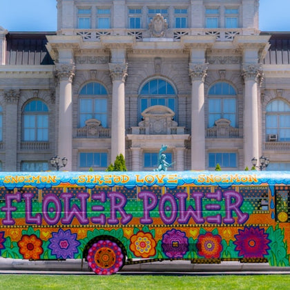 A colorful bus with 'Flower Power' painted on it, parked in front of a large historic building with ornate details.