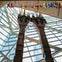 Tall metal beams on display inside a building with a glass ceiling and flags hanging above.