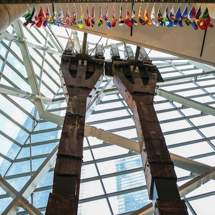Tall metal beams on display inside a building with a glass ceiling and flags hanging above.