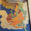 A mosaic artwork depicting a green figure surrounded by orange and yellow flames against a blue and yellow background.